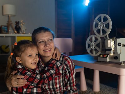 Mother and daughter watching old movie on retro vintage film projector at home